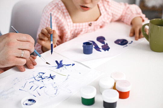 Cropped photo of girl with Down syndrome drawing on a paper with blue paints