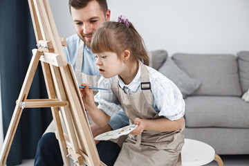 Girl with Down syndrome and her father painting on an easel with brushes