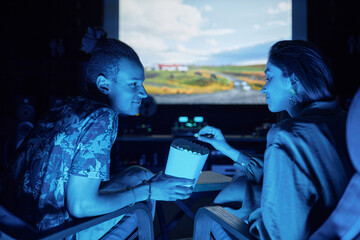 Side view portrait of young couple watching movie together on big screen in home cinema and eating popcorn