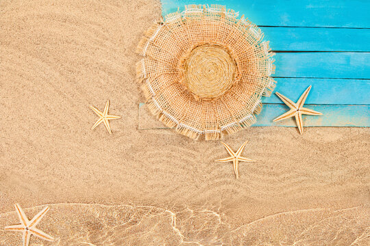 Flat lay composition with beach accessories on wooden pier by water. Straw hat, starfish and blue boards by sea on sand. Summer, vacation, tourism in hot country. Copy space