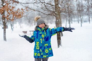 winter portrait of cute caucasian boy on sunny day playing snowballs