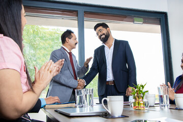 Indian corporate boss handshaking and appreciating employee for doing good work in company standing at conference room.