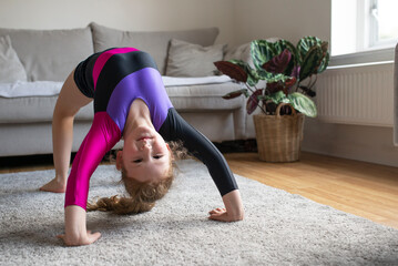 Pretty young girl in gymnastics leotard sportswear doing fitness exercises at home, yoga, stretching