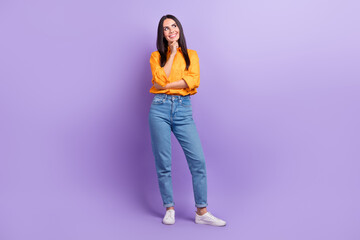 Full length photo of satisfied minded good mood girl dressed yellow shirt pants look at empty space isolated on purple color background