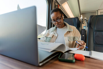 Modern business woman in the train traveling to work. Young woman writing down in notebook. Modern and fast travel concept.