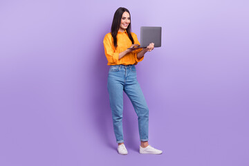 Full length photo of intelligent clever girl dressed yellow shirt pants look at laptop writing letter isolated on purple color background