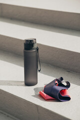 Gray sport bottle drinking water flask and gymnastic elastic bands on white stair. Hydration or thirst during fitness