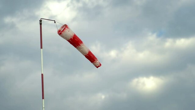 Windsock indicator of wind on runway of an airport, showing the direction and force of the wind against the cloudy blue sku