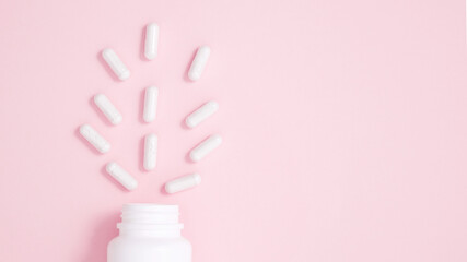 White bottle container with medication capsules on pink background. Concept of healthcare and medicine. Top view, copy space