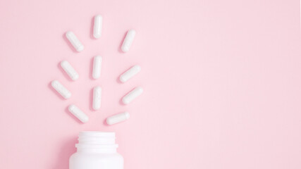 White bottle container with medication capsules on pink background. Concept of healthcare and...