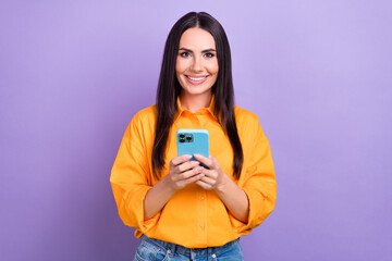 Photo of pleasant lovely girl with straight hairdo dressed yellow shirt hold smartphone chatting isolated on purple color background