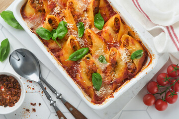 Cannelloni or conchiglioni. Baked stuffed pasta shells with bolognese meat sauce, tomatoes, basil on white tile modern table. Traditional Italian bolognese baked pasta with parmesan. Italian cuisine.