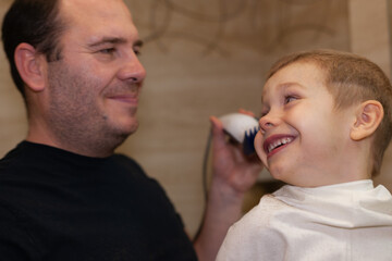 Hairdresser at home. Dad cuts son's hair at home. The son is smilling