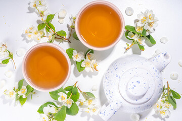 Organic herbal health drink. Jasmine flowers green tea, in white mugs, with teapot, on white table, with blooming jasmine flowers 