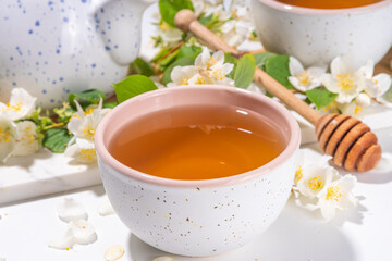Organic herbal health drink. Jasmine flowers green tea, in white mugs, with teapot, on white table, with blooming jasmine flowers 