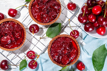 Cherry dessert tartlets. Mini tarts with cream filling and cherry topping, summer traditional pie, with fresh cherries on white wooden background