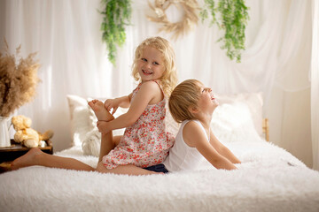 Cute sweet toddler children, tickling feet on the bed, laughing and smiling - obrazy, fototapety, plakaty