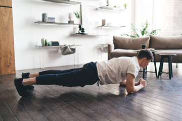 Male athlete practicing forearm plank exercise in apartment