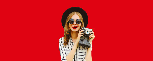 Summer portrait of happy smiling young woman photographer with film camera wearing black round hat...