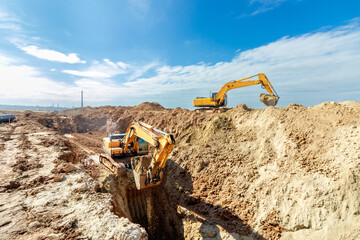 Two Excavator are digging soil in the construction site on sky background,with white fluffy cloud