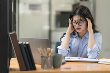 Asian businesswoman are serious at work causing headaches and stressed out with documents with a laptop at the office.