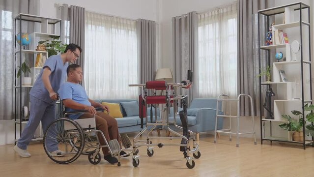 Full Body Side View Of Asian Male Nurse Helping Patient In Wheelchair Learning To Use Walker To Stand By Himself During A Physical Therapy At Home
