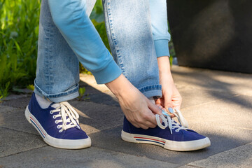 woman tying shoelaces on sneakers sitting on a bench