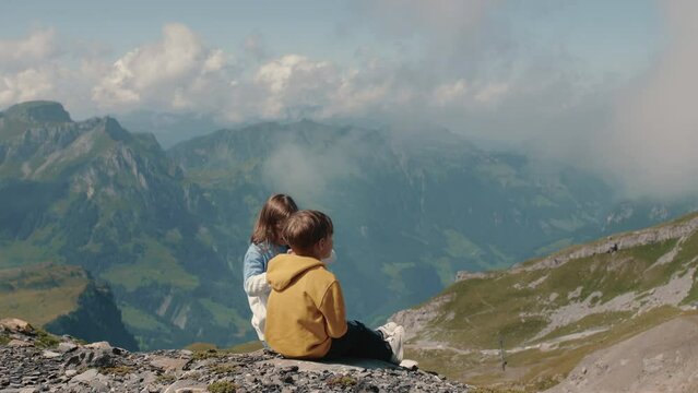 Cinematic shot of tenage boy and girl observing together picturesque panorama of Swiss mountains