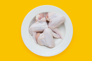 Fresh raw chicken wings in white plate on yellow background.