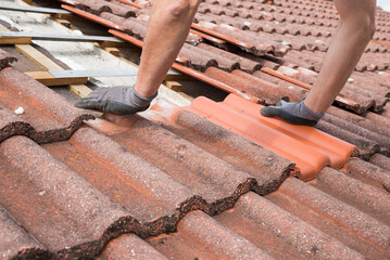 man replaces broken roof shingles on the rooftop with new ones