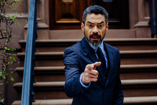 businessman pointing at camera, serious hispanic man with beard, outdoors,