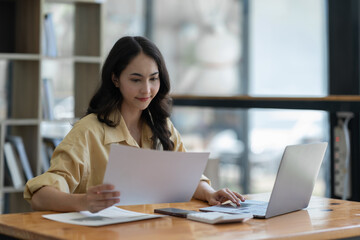 Confident Asian businesswoman using laptop calculator Paperwork for financial work, calculations on the desk, tax, report, accounting, statistics. Analytical research concept.