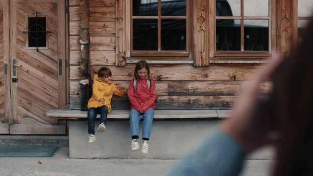 Teen boy and girl, sitting in front of wooden hut and posing together. Brother huggs sister. Strong facial emotions.