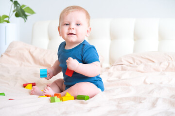 baby boy in blue bodysuit playing with colorful wooden eco toys on bed