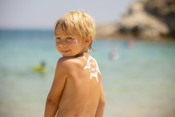 Happy child, blond boy on the beach with applied sun screen,  enjoying summer, playing. Chalkidiki