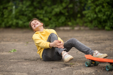 a child with an injury near his penny board or skateboard outdoors. The girl fell on the asphalt next to her penny board and is holding on to her sore leg. © KatrinaQQ