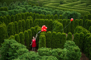 Balloons drift away from a young woman in a garden maze; Luray, Virginia, United States of America