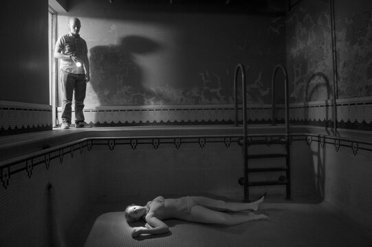 Teenage girl appears to lie dead in an empty swimming pool as a man looks on; Lincoln, Nebraska, United States of America