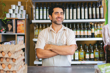 Latin man greengrocer in an organic grocery shop behind the counter with his arms crossed looking...