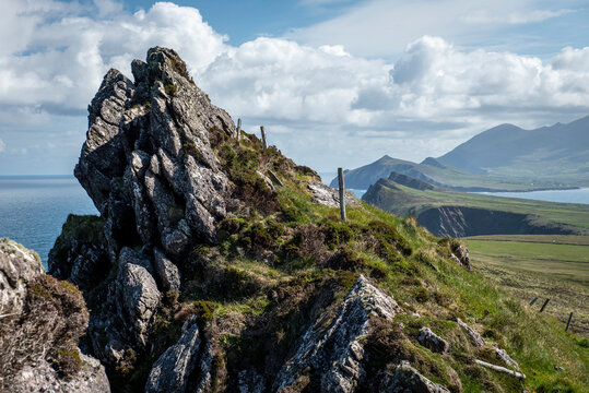 Close-up of a rocky, sea cliff outlook with a distant view from Sybil Head of the Three Sisters mountain peaks along the Atlantic Coast on Dingle Peninsula; County Kerry, Ireland
