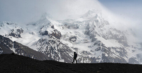 Silhouette of a person walking along a glacial moraine in front of a large snow-capped mountain on the South Coast of Iceland; South Iceland, Iceland