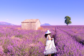 Une mariée habillée en blanc avec un chapeau dans un paysage magnifique, au milieu d'un champ de lavande dans le Luberon,  pendant un voyage pendant les vacances en été dans le Sud de la France - obrazy, fototapety, plakaty