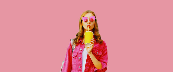 Portrait of stylish modern young woman drinking fresh juice wearing jacket, sunglasses on pink...