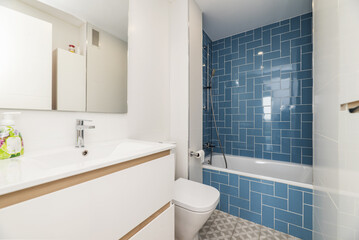 Fototapeta na wymiar Bathroom with white porcelain sink under frameless mirror and walk-in shower with tub and blue tile