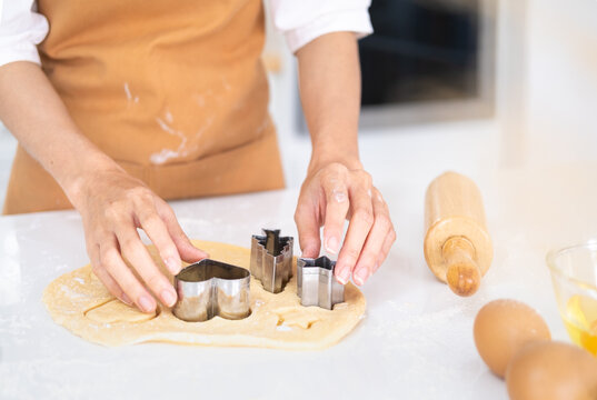 Cropped image of hands cutting cookies of dough while baking in kitchen .Making for homemade biscuits. On the table is dough and a set of cookie molds with other kitchen equipment.
