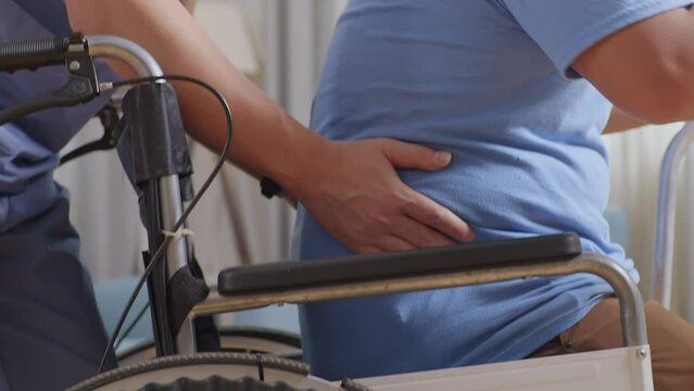 Close Up Of Male Nurse Helping Patient Who In A Wheelchair To Stand Up By A Walker During A Physical Therapy At Home
