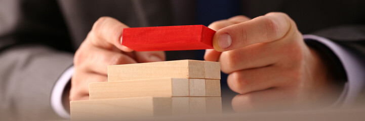 Businessman hand builds ladder from wooden blocks on top of red color. Achieving goals successful career and leadership concept
