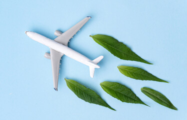 Sustainable Aviation Fuel. White airplane model, fresh green leaves on blue background.