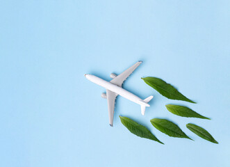 Sustainable Aviation Fuel. White airplane model, fresh green leaves on blue background.