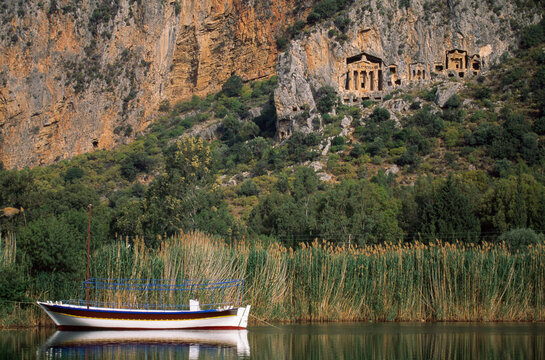 Sailboat anchored in the Dalyan river beneath Lycian rock tombs; Kaunos, Turkey